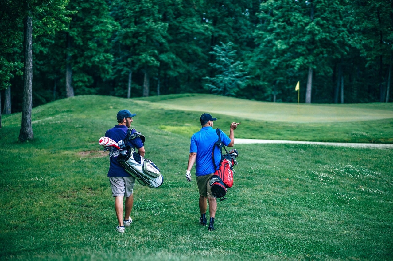 Two men walking across a bright green golf course carrying bags.